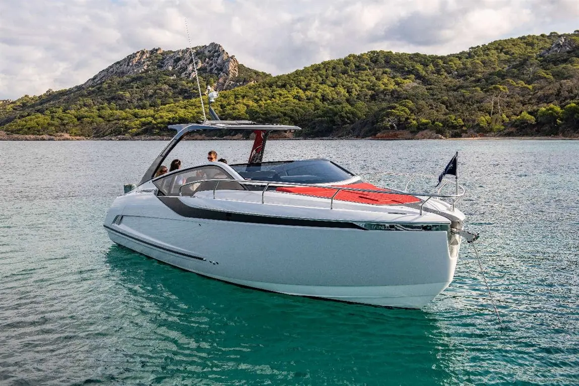 A sleek white motorboat anchored in clear water, surrounded by lush green hills and cloudy skies, with three people onboard.